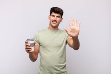 Kahveli genç adam gülümsüyor ve arkadaş canlısı görünüyor, 5 ya da 5 numarayı gösteriyor, eli önde, geri sayıyor.