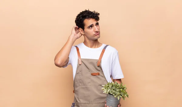 young gardener man feeling puzzled and confused, scratching head and looking to the side