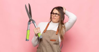 Genç sarışın kadın şaşkın ve şaşkın hissediyor, başını kaşıyor ve yan tarafa bakıyor.