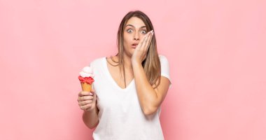 Genç sarışın kadın şok olmuş ve korkmuş hissediyor, ağzı açık ve elleri yanaklarında korkmuş görünüyor.