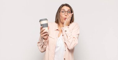 Genç sarışın kadın şok olmuş ve korkmuş hissediyor, ağzı açık ve elleri yanaklarında korkmuş görünüyor.