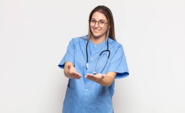 Genç sarışın kadın mutlu bir şekilde gülümsüyor arkadaş canlısı, kendinden emin, olumlu bakışlı, bir nesne ya da konsept sunuyor ve gösteriyor.