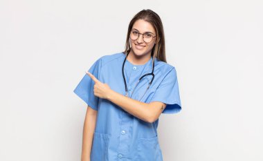 Genç sarışın kadın neşeyle gülümsüyor, mutlu hissediyor ve kenarı ve yukarıyı işaret ediyor, fotokopi uzayındaki nesneleri gösteriyor.