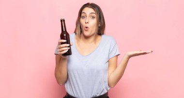 Genç sarışın kadın şaşırmış ve şoka uğramış görünüyor. Çenesi düşmüş ve eli açık bir objeyi tutuyor.