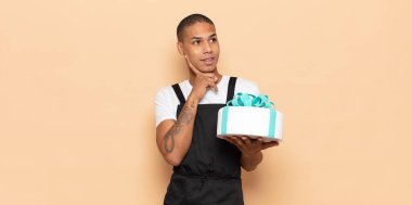 Genç siyah adam mutlu bir şekilde gülümsüyor ve hayal kuruyor ya da şüphe ediyor.