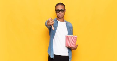 Genç siyahi adam kızgın, sinirli, hayal kırıklığına uğramış ya da canı sıkkın, ciddi bir bakışla başparmağını kaldırıyor.