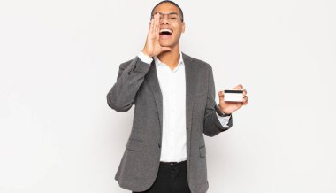 Genç siyah adam mutlu, heyecanlı ve pozitif hissediyor. Elleri ağızda, bağırarak bağırıyor.