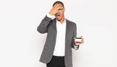 Genç siyahi adam şok olmuş, korkmuş ya da korkmuş görünüyor. Yüzü elle kaplanmış ve parmaklarının arasından gizlice bakıyor.