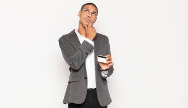 Genç siyahi adam düşünüyor, kuşkulu ve şaşkın hissediyor, farklı seçeneklerle, hangi kararı vereceğini merak ediyor.