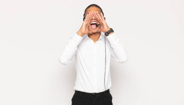 Genç siyah adam mutlu, heyecanlı ve pozitif hissediyor. Elleri ağızda, bağırarak bağırıyor.