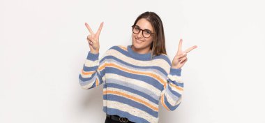 Genç sarışın kadın gülümsüyor ve mutlu görünüyor, arkadaş canlısı ve memnun, işaret eden zafer ya da huzur iki elinle