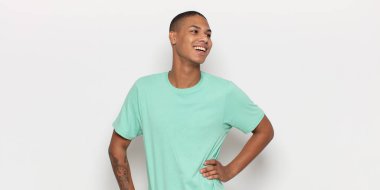 Genç siyah adam mutlu, neşeli ve kendinden emin görünüyor. Gururla gülümsüyor ve iki elini de kalçasında istiyor.