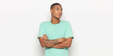 Genç siyahi adam omuz silkiyor, kafası karışık ve kararsız, kolları bağlı ve şaşkın bir şekilde bakıyor.