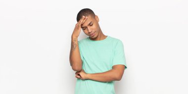 Genç siyahi adam stresli, utanmış ya da üzgün görünüyor, baş ağrısı var, yüzü elle kapatılmış.