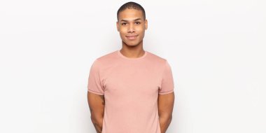 Genç siyah adam pozitif ve kendinden emin gülümsüyor. Tatmin olmuş, arkadaş canlısı ve mutlu görünüyor.