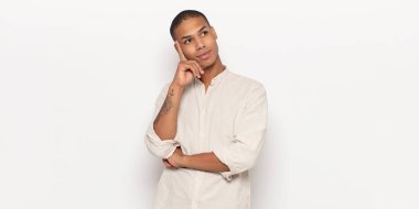 Genç siyah adam mutlu bir şekilde gülümsüyor ve hayal kuruyor ya da şüphe ediyor.