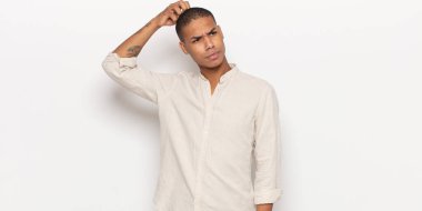 Genç siyah adam şaşkın ve şaşkın hissediyor, başını kaşıyor ve yana bakıyor.