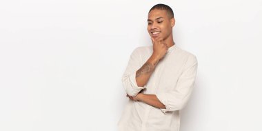 Genç siyahi adam mutlu, kendinden emin bir ifadeyle gülümsüyor, elleri çenesinde, merak ediyor ve yan tarafa bakıyor.