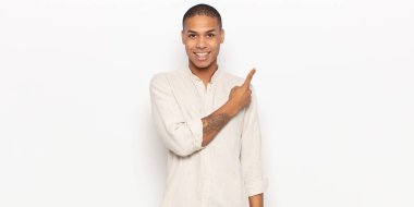 Genç siyah adam neşeyle gülümsüyor, mutlu hissediyor ve kenarı ve yukarıyı işaret ediyor, fotokopi uzayındaki nesneleri gösteriyor.