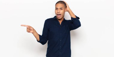 Genç siyahi adam gülüyor, mutlu, pozitif ve şaşırmış görünüyor. Yan fotokopi alanını işaret eden harika bir fikrin farkına varıyor.