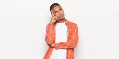 Yoğunlaşmış bakışlı genç siyahi adam şüpheli bir ifadeyle yukarı ve yana bakıyor.