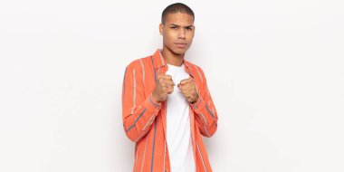 Genç siyah adam kendinden emin, sinirli, güçlü ve agresif görünüyor. Yumrukları boks pozisyonunda dövüşmeye hazır.