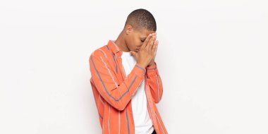 Genç siyahi adam, üzgün, hayal kırıklığına uğramış bakışlarıyla gözleri kapatıyor, ağlıyor, yan gözle bakıyor.