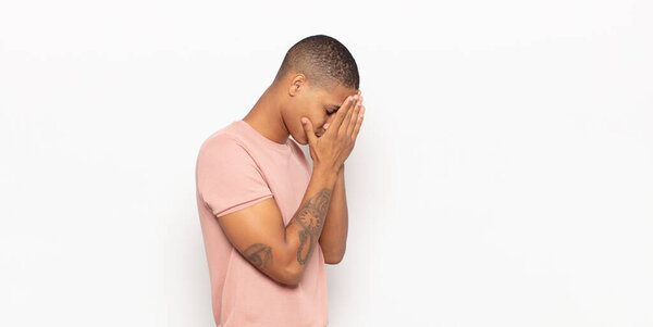 young black man covering eyes with hands with a sad, frustrated look of despair, crying, side view