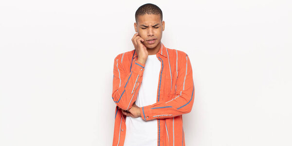 young black man holding cheek and suffering painful toothache, feeling ill, miserable and unhappy, looking for a dentist