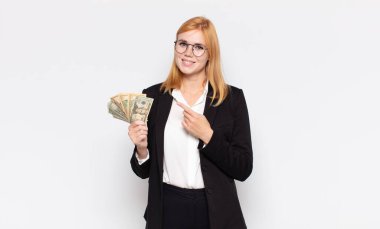 Güzel bir kadın neşeyle gülümsüyor, mutlu hissediyor ve kenarı ve yukarıyı işaret ediyor, fotokopi uzayındaki nesneleri gösteriyor.