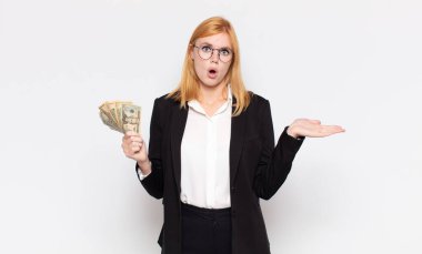 Güzel bir kadın şaşırmış ve şoka uğramış görünüyor, çenesi düşmüş, elinde açık bir elle bir nesne tutuyor.