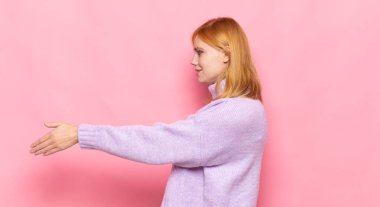 Kızıl saçlı güzel kadın gülümsüyor, seni selamlıyor ve başarılı bir anlaşma için el sıkışmayı teklif ediyor, işbirliği konsepti.