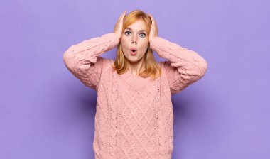 Kızıl saçlı güzel bir kadın heyecanlı ve şaşırmış görünüyor, ağzı açık, iki eli başında, kendini şanslı hissediyor.