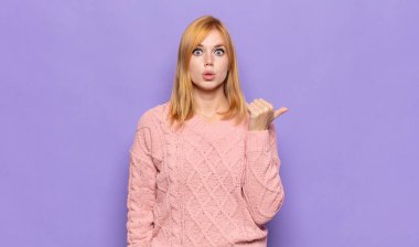 Kızıl saçlı güzel bir kadın inançsızlıktan şaşkın şaşkın bakıyor, yan taraftaki objeyi işaret ediyor ve 