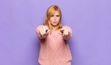 Kızıl saçlı, güzel bir kadın kamerayı iki parmağıyla ve kızgın bir ifadeyle sana görevini yapmanı söylüyor.