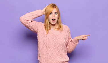 Kızıl saçlı güzel bir kadın gülüyor, mutlu, pozitif ve şaşırmış görünüyor, yanal fotokopi alanını gösteren harika bir fikri fark ediyor.