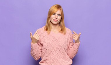 Kızıl saçlı, kötü tavırlı, gururlu ve agresif görünen, yukarıyı gösteren ya da ellerinle alay eden güzel bir kadın.