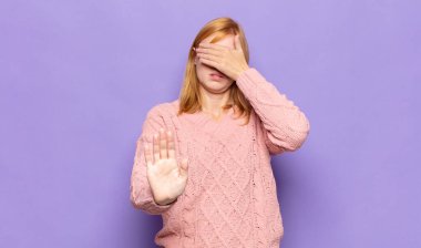 Kızıl saçlı güzel bir kadın yüzünü eliyle kapatıyor ve kamerayı durdurmak için diğer elini öne koyuyor, fotoğraf ya da resimleri reddediyor.