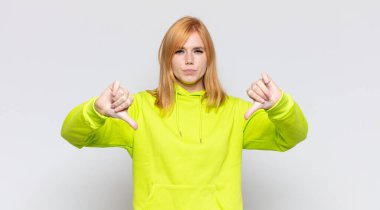 Kızıl saçlı, güzel bir kadın üzgün, hayal kırıklığına uğramış ya da kızgın görünüyor, anlaşmazlık içinde başparmaklarını gösteriyor, hayal kırıklığına uğramış hissediyor.