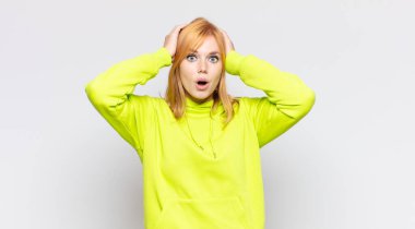 Kızıl saçlı güzel bir kadın heyecanlı ve şaşırmış görünüyor, ağzı açık, iki eli başında, kendini şanslı hissediyor.