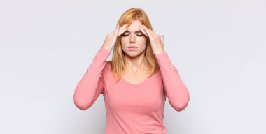 Kızıl saçlı güzel bir kadın stresli ve hayal kırıklığına uğramış görünüyor, baskı altında çalışıyor ve başı ağrıyor.