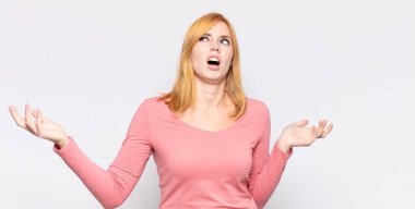 red head pretty woman shrugging with a dumb, crazy, confused, puzzled expression, feeling annoyed and clueless