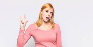 Kızıl saçlı güzel bir kadın mutlu, eğlenceli, kendinden emin, pozitif ve asi, elle rock veya heavy metal işareti yapıyor.