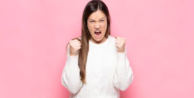 Genç, güzel bir kadın sinirli, sinirli, kızgın bakışlar ve sıkı yumruklar ile agresif bir şekilde bağırıyor.