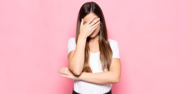 Genç, güzel bir kadın stresli, utanmış ya da üzgün görünüyor. Baş ağrısı var, yüzü elle kapatılmış.