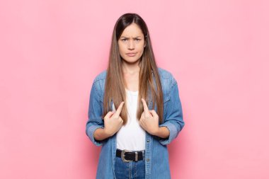 Genç ve güzel bir kadın, şaşkın ve şaşkın bir bakışla kendini işaret ediyor, seçildiğine şaşırmış ve şaşırmış.