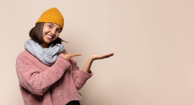 Genç bir kadın mutlu, kendinden emin ve güvenilir görünüyor. Gülümsüyor ve zafer işareti gösteriyor. Olumlu bir tavırla.