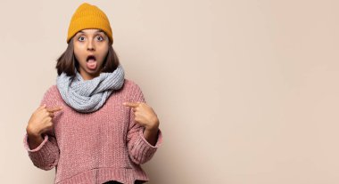 Genç bir kadın şaşkın ve şaşkın bir bakışla kendini işaret ediyor. Seçildiğine şaşırmış ve şaşırmış.