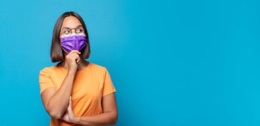 Gülümseyen mutlu, kendine güvenen bir yüz ifadesi olan genç bir kadın. Elleri çenesinde, merak ediyor ve yan tarafa bakıyor.