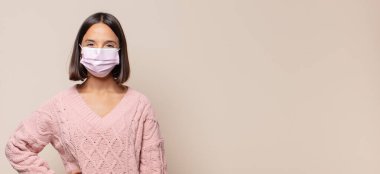 Genç bir kadın mutlu bir şekilde gülümsüyor, eli kalçasında ve kendinden emin, olumlu, gururlu ve arkadaş canlısı.